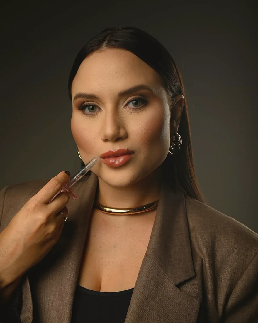 Dra. Lorena Ferreira em retrato de estúdio, de blazer marrom e gargantilha dourada, olhando para a câmera